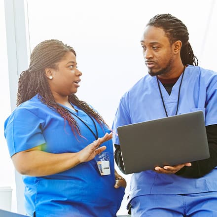 A male and female nurse working on a laptop while discussing how long it takes to become a nurse