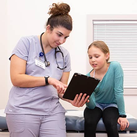 A family nurse practitioner explaining something with a tablet to her patient, a child.
