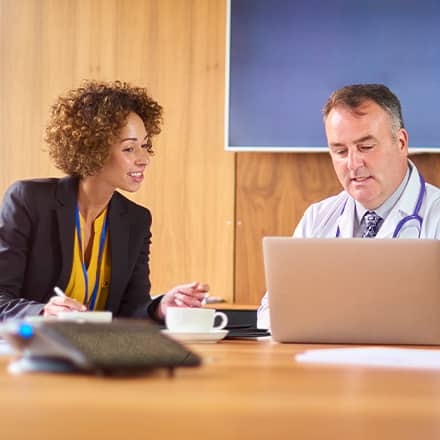 A public health professional discussing a project with a doctor as they both look at a laptop