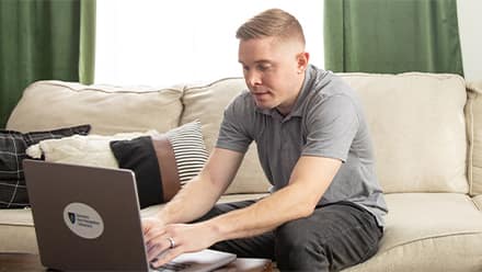 Rob Thomas, a 2024 graduate from SNHU, sitting on a couch and typing on a laptop.