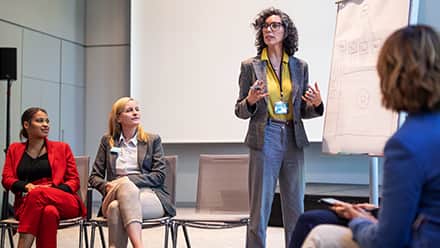 An industrial-organizational psychologists standing at the front of the room presenting to other psychologists.