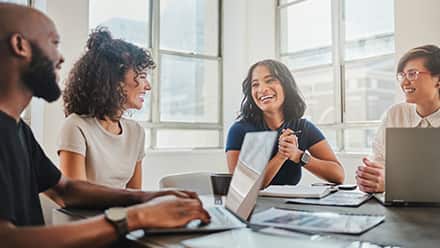 A group of smiling professionals sat around a conference table with laptops and documents.