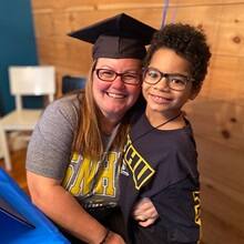 Laura Gaughan wearing her graduation cap and an SNHU shirt, hugging one of her sons who is also wearing an SNHU shirt.