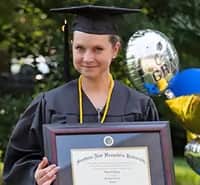 Loretta Gray, an SNHU graduate and Virginia resident, holding her framed diploma and wearing her cap and gown.