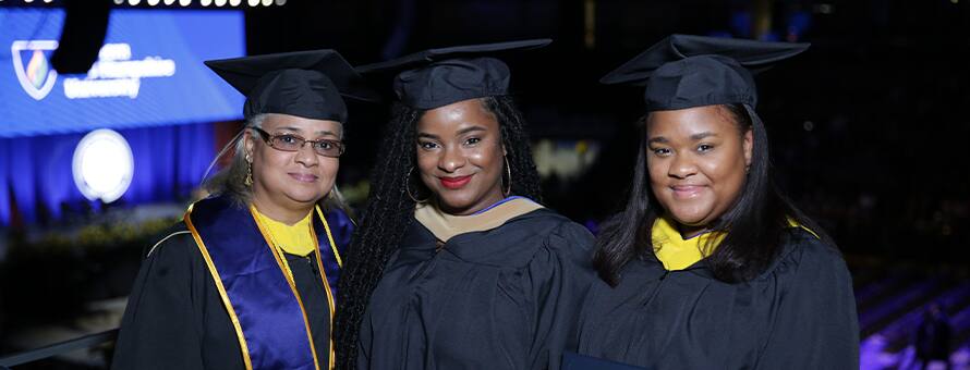 SNHU graduate and Georgia resident Kellann Alves standing between her mother Sabrina Mentis and sister Stephanie Mentis, all wearing their cap and gowns.