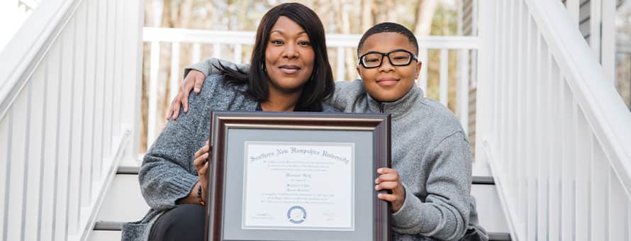A mother holding her diploma and sitting next to her son