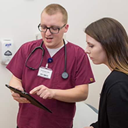 A nurse pointing to his clipboard and speaking with a patient.