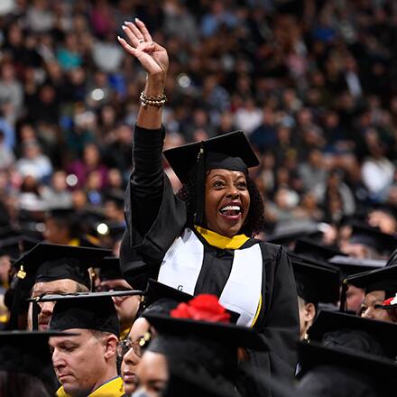 A graduate dressed in cap and gown, waving to loved ones at an SNHU Commencement ceremony.