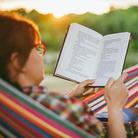 A woman sitting in a hammock during the summer reading her favorite book