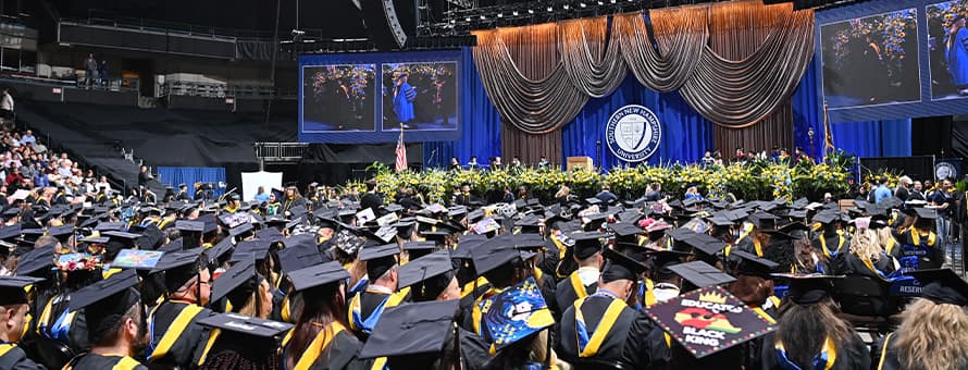 A crowd of seated graduates from the SNHU class of 2025, looking at the stage at the SNHU Arena.