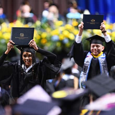Two SNHU graduates holding up their diplomas at the Fall 2025 commencement ceremony.