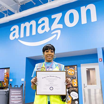 SNHU graduate, Remy Twine, standing in an Amazon facility holding her SNHU diploma.