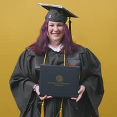 Amber Bownan, an associate in liberal arts and bachelor's in general studies graduate from SNHU wearing her cap and gown in front of a yellow background.