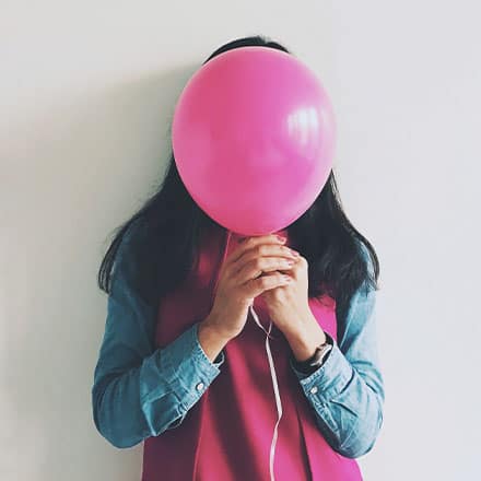 A woman holding pink balloon in front of her face.