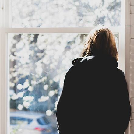 A person leaning against a window frame, considering the barriers to mental health awareness and treatment.