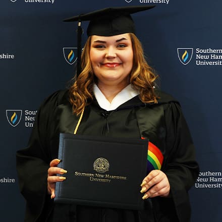 Ashley Smith, a 2024 SNHU graduate who earned her bachelor's in communication wearing her cap and gown in front of a dark blue background.