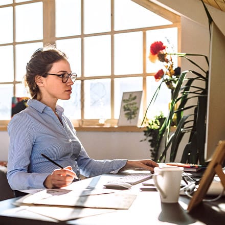 An online instructor sitting at a desk and looking at a computer as she video conferences with an online student.