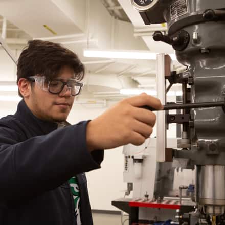 A STEM major wearing goggles and working with machinery. 