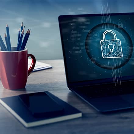A laptop with a lock on its screen sitting on a desk by a notebook and cup of pencils.