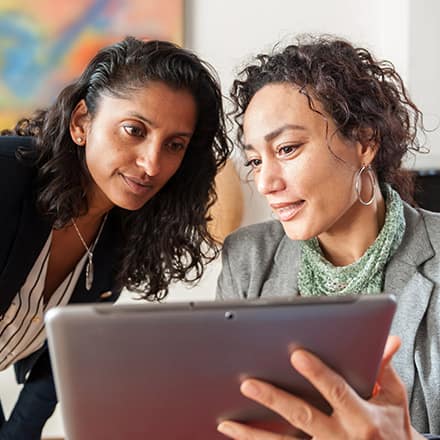 Two business professionals looking at a tablet and considering the best reasons for getting an MBA Degree.