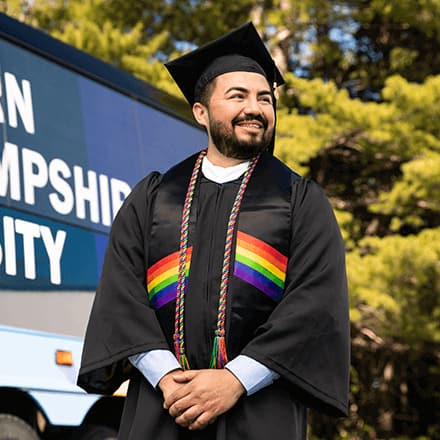 Jesús Suárez wearing his cap and gown in front of the Southern New Hampshire University bus