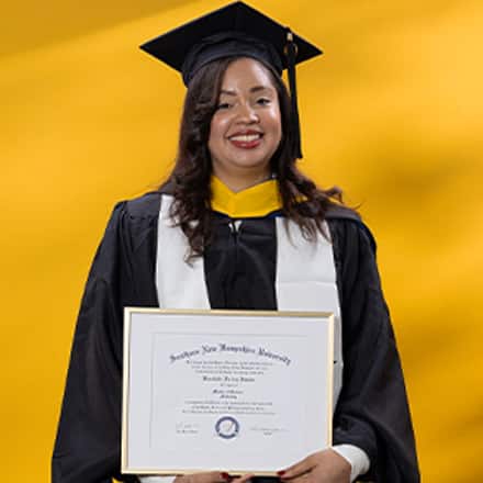 Brendaliz De Los Santos dressed in a graduation cap and gown, holding her SNHU diploma after finishing her master's in marketing.