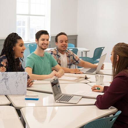 A group of college students at a large table covered with notebooks and laptop computers.