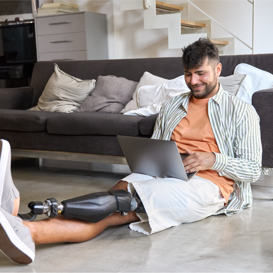 A young man with a prosthetic leg, using a laptop while sitting.