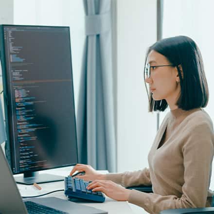 A cybersecurity professional typing on a keyboard in front of a large monitor of code.