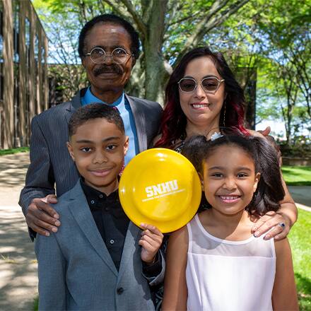 David Balogun standing with his family holding an SNHU frisbee