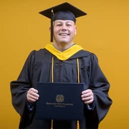 David Wallace, a 2025 SNHU graduate who earned his bachelors in business administration wearing his cap and gown in front of a yellow background.