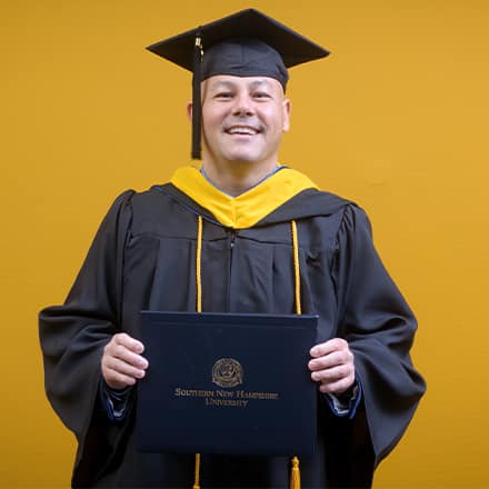 David Wallace, a 2025 SNHU graduate who earned his bachelors in business administration wearing his cap and gown in front of a yellow background.