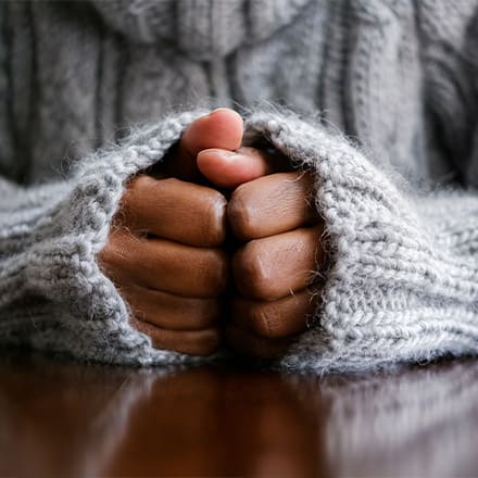 Someone's hands curled in a gray knit sweater as they manage their anxiety
