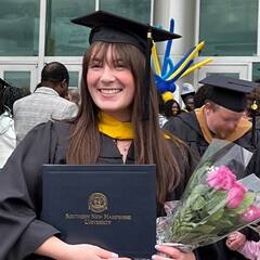 Emily Bevens, a 2023 SNHU graduate who earned her master's in psychology with a concentration in forensic psychology, standing outside her commencement ceremony in her cap and gown, holding her diploma.