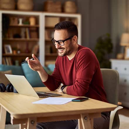 A man sitting at a desk smiling and working on his laptop while earning an English degree.