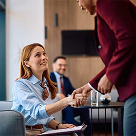 A professionally dressed woman shaking someone's hand in an office setting to represent entry-level HR jobs.