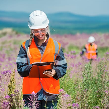 Environmental scientists in a field wearing protective equipment and taking notes.