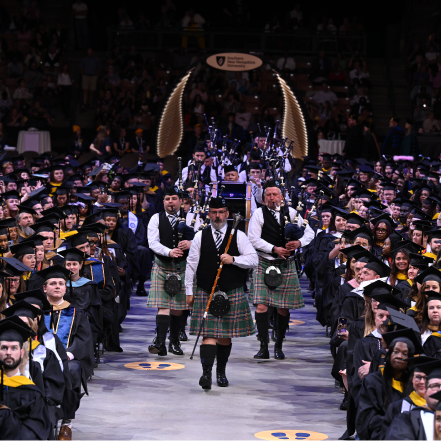 Rows of graduating students as a procession of bagpipers go down center aisle during Fall commencement ceremony.
