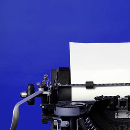 The upper left corner of an old fashioned typewriter with a blank sheet of paper loaded and clipped in place.