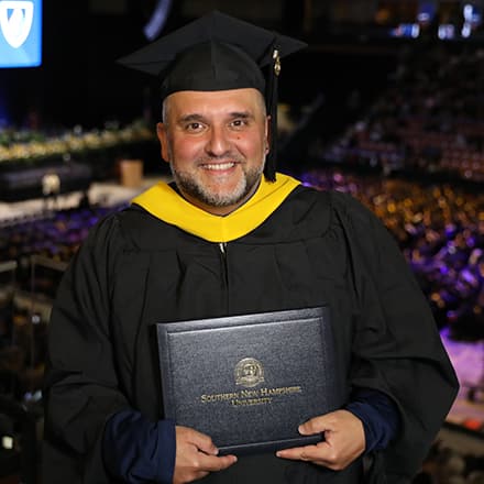 SNHU master's in higher education administration graduate Frederico Curty in his cap and gown and holding his diploma at the SNHU commencement ceremony.