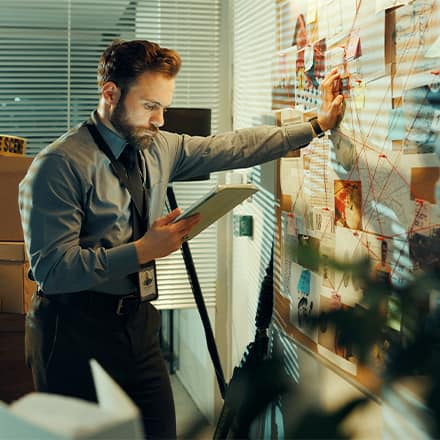 A detective with a criminal justice degree, leaning against a map and reviewing a case file in his hand.