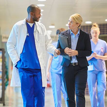 A healthcare administrator speaking with a doctor as they walk down a hospital hallway.