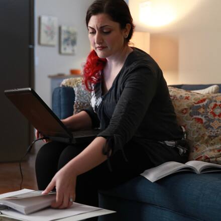 A master’s student sitting on the couch with a laptop and books, considering how long it will take her to finish her degree program.