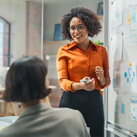 A marketing manager presenting ideas on a whiteboard during a team meeting while colleagues listen.
