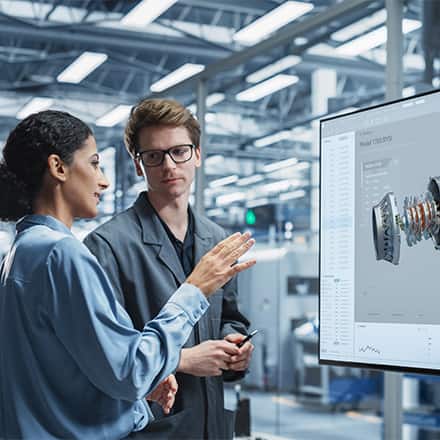 An engineering manager listening to an engineer explaining machinery on a screen.