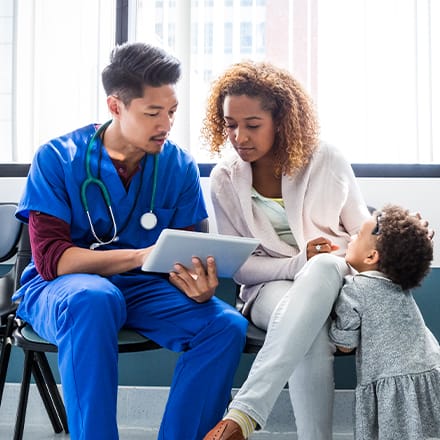 A CNA sitting with a patient and a small child, explaining something on a tablet