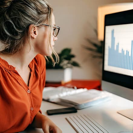 A professional who learned how to become a data analyst, sitting in front of a computer with a bar graph on the screen.