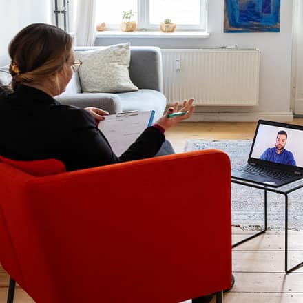 An online therapist taking notes on a clipboard while on a video call with a client.