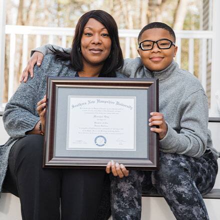 A mother holding her diploma and sitting next to her son
