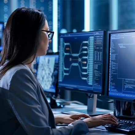 A woman sitting in front of two computer monitors after she learned how to become a cyber security professional.  